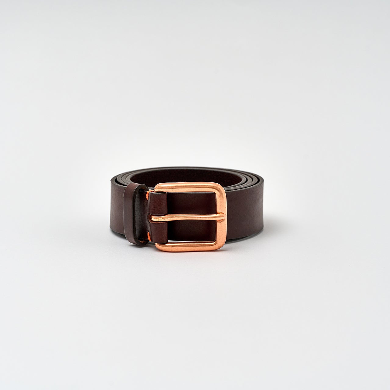 Brown leather belt with a rose gold buckle on a light gray background